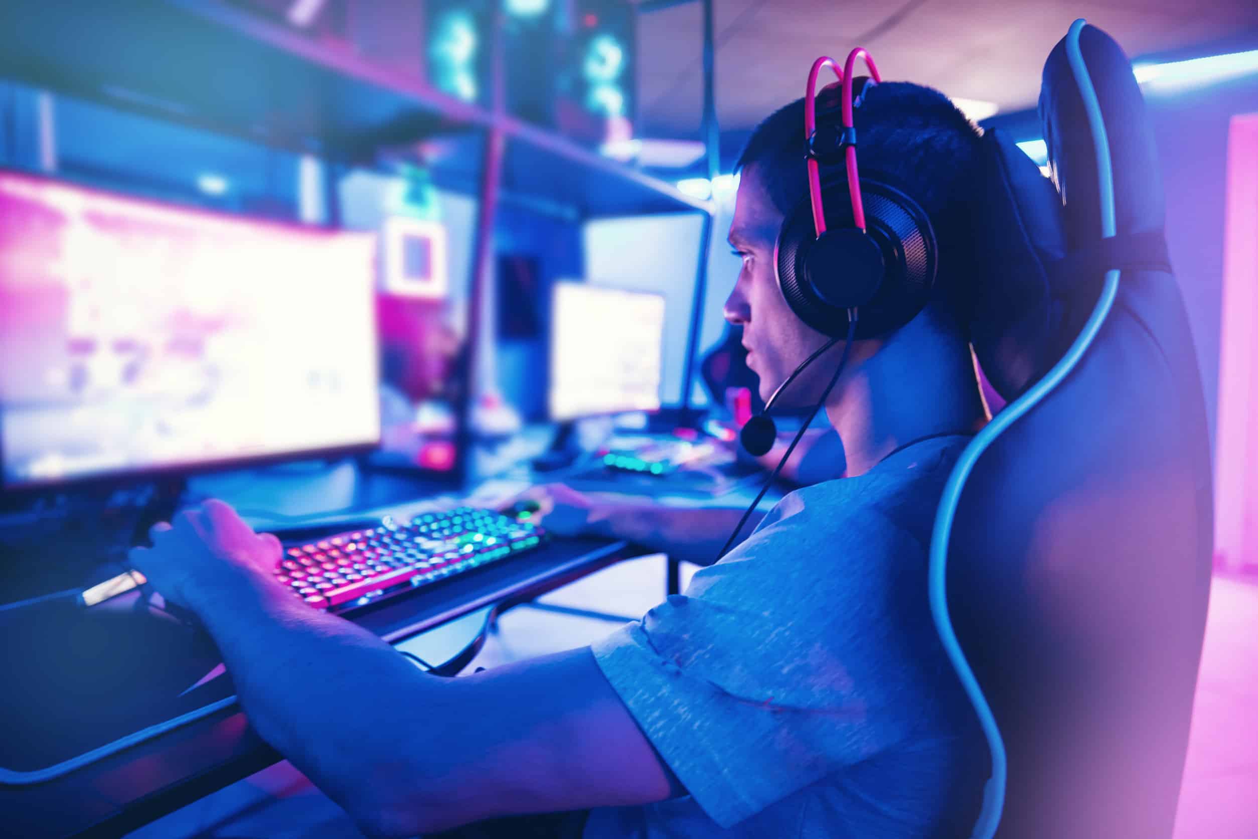 Young man gamer play online video games with headphones in internet club cafe blue color Esports concept